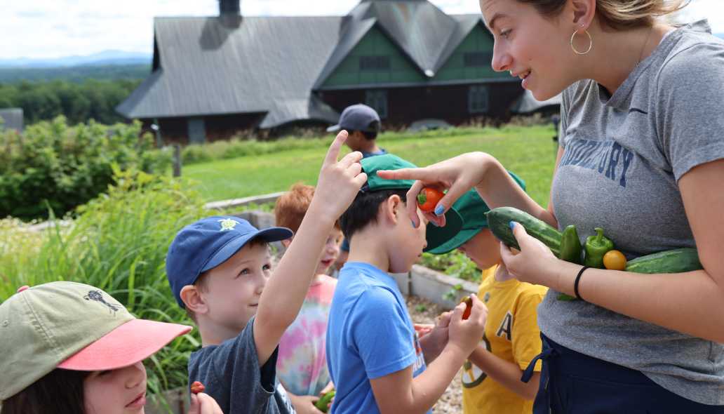 a summer camp educator looks at a garden harvest with campers